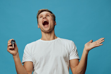 Joyful man celebrating happiness, holding car key, expressing excitement in casual white t-shirt...