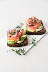 Smoked salmon avocado sandwich on light background. Black whole grain bread, avocado, salted salmon and dill for healthy breakfast