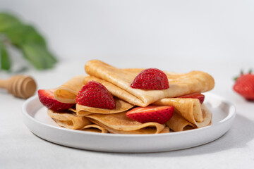 Thin crepes with strawberries in plate on light background. Morning breakfast concept