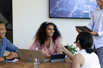In office, diverse team collaborating using laptops and tablets in meeting
