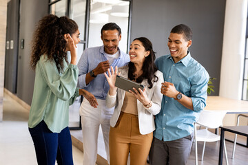 Business team collaborating and laughing while using tablet in modern office