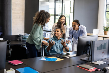 Collaborating around computer, diverse business team discussing ideas in modern office