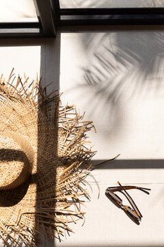 Overhead shot of stylish artisanal straw hat and tortoiseshell sunglasses at a luxury hotel resort with shadows of architectural windows and palm fronds. 