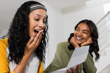 Excited African American woman reading letter while friend smiles at home