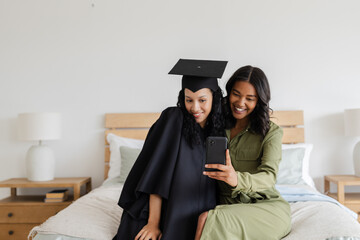 Graduation day, African American mother and daughter taking selfie on bed, smiling