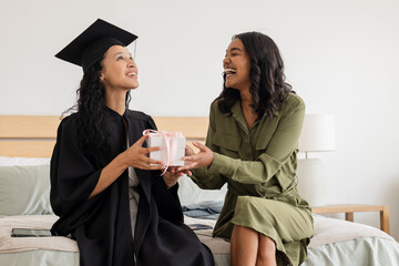Graduation celebration, Asian mother giving gift to daughter in cap and gown