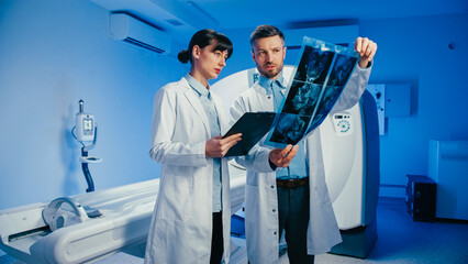 Charming female radiologist pointing at brain scan while holding clipboard. Male doctor raising...
