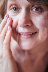 Fototapeta premium Close-up of the face of a mature woman applying a moisturizing white cream. An elderly lady takes care of her facial skin. A pensioner with a serum.