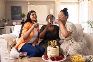 Celebrating at home, diverse women enjoying drinks with birthday cake and snacks