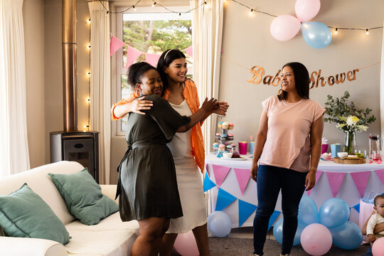 Celebrating baby shower, diverse women hugging and smiling in decorated living room - Powered by Adobe