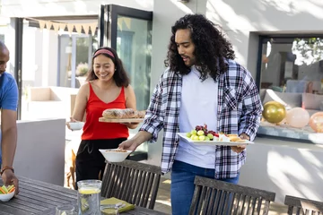Selbstklebende Fototapeten Friends setting outdoor table with food, preparing for festive celebration © wavebreak3