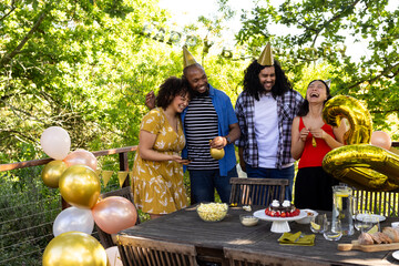 Celebrating birthday outdoors, friends wearing party hats and holding balloons, laughing