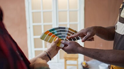 Pair of hands holding and displaying a fan deck of paint color samples in well-lit space with white door in background, indicating possible color choices for interior design
