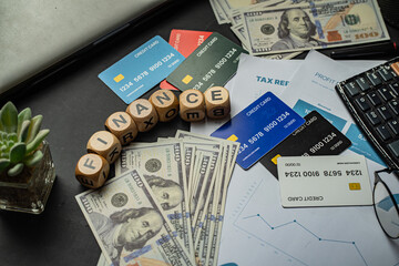 Business and finance background image showing a blend of paper currency, credit cards, profit charts, tax files, and an office setup. The word “FINANCE” arranged with wooden letter blocks.