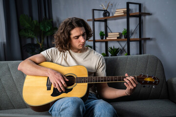Obraz premium Young Man Practicing Acoustic Guitar at Home on a Cozy Couch