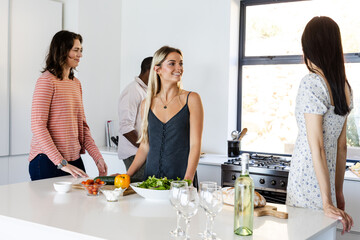 In modern kitchen, friends preparing meal and having conversation together