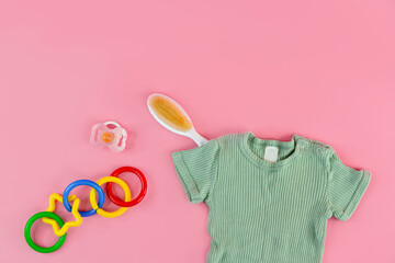 A layout with baby clothes and other baby accessories for a newborn on a pink background, top view.