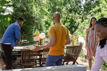 Setting table outdoors with balloons, African American friends preparing festive celebration