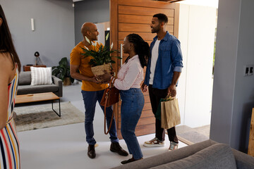 Welcoming friends at home, African American couple bringing gifts and plant