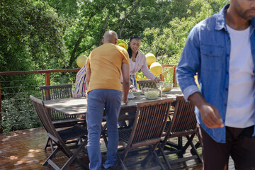 Setting up outdoor table, African American friends celebrating together on sunny day