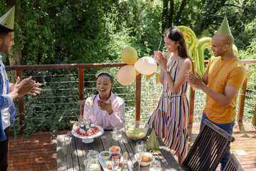 Friends clapping as African American woman blows candles celebrating birthday outdoors
