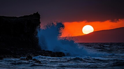 The ocean waves crash against a dark rocky cliff at sunset