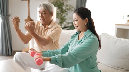 Obraz premium Happy elderly couple exercising together with dumbbells at home, focusing on muscle strength, joint health, and physical wellness for improved mobility and healthy aging. Retirement concept. Myrmidon.