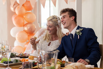 Bride and groom laughing together at wedding reception table with food and drinks