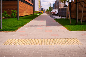urban sidewalk with tactile paving for accessibility, featuring modern architecture and greenery. brick walkway enhances cityscape design, providing safe navigation for visually impaired people
