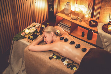 Hot stone massage at spa salon in luxury resort with warm candle light, blissful woman customer...