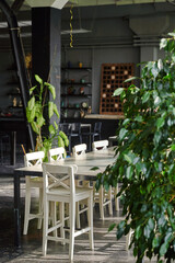 loft cafe interior featuring rustic dining table and white chairs with lush indoor plants. natural light floods space, creating cozy ambiance perfect for gatherings or work.