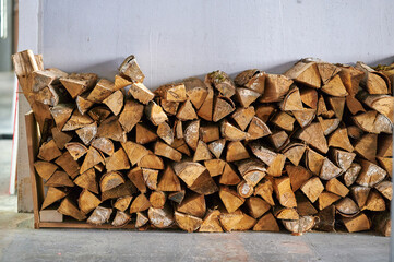 stacked firewood creating rustic charm for winter warmth in home or cabin setting. natural, raw logs piled neatly against light wall, ideal for cozy ambiance enthusiasts