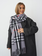 Stylish woman in gray coat and scarf showcasing winter fashion in a studio setting