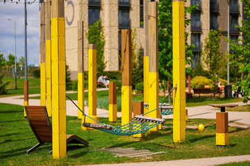 Fototapeta premium modern playground with yellow structures and net hammock provides urban oasis amid apartment buildings. green lawn and benches create vibrant community gathering space