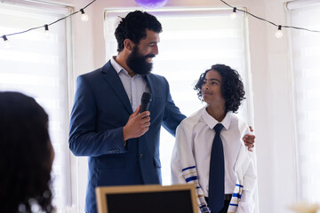 Celebrating son's bar mitzvah, father speaking into microphone at home