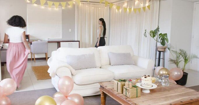 Two happy multiracial female friends preapring food and decorations for a baby shower party in livin