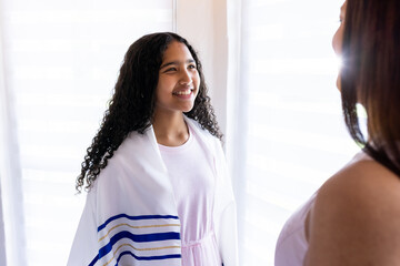 Young girl wearing prayer shawl smiling at woman during bar mitzvah