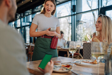 Waitress holding pos terminal accepting mobile payment from customer in restaurant