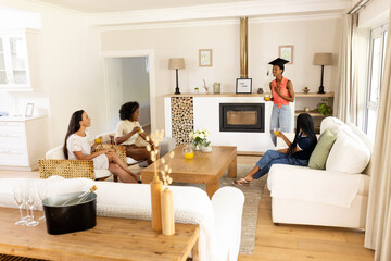 Fototapeta premium Celebrating graduation, diverse female friends enjoying drinks in cozy living room