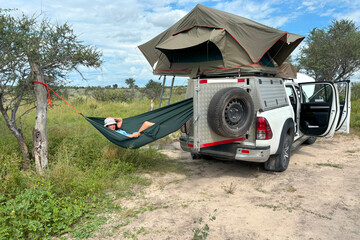 A dark-haired woman in a safari outfit relaxes in a hammock in the African wilderness. Adventure in the Central Kalahari, Botswana. 