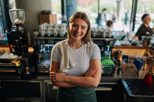 Smiling barista with crossed arms in coffee shop - Powered by Adobe