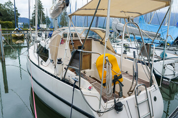 Sailboat docked at marina surrounded by clear water and multiple masts on a cloudy day
