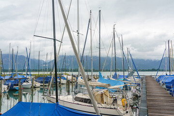 Sailboats docked at a marina with scenic mountains and cloudy skies in late afternoon