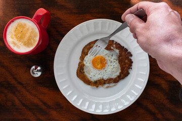 Cheesecake topped with a fried egg, coffee, salt shaker, hand