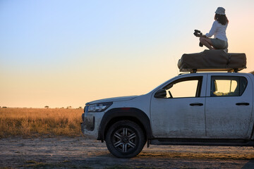 Solo Woman Safari Overlander Enjoying Golden Hour on Self-Drive Safari in African Wilderness at Sunset.