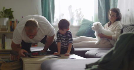 Fototapeta premium Family spending time together in cozy living room, grandfather playing with young boy, mother smiling with pet dog on couch, warm and homely atmosphere, bonding moment