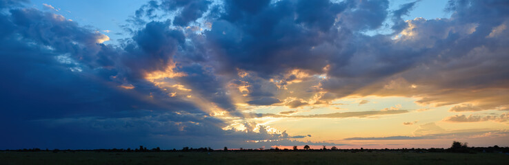 Golden sunset with dramatic sunbeams and colorful clouds over Nxai Pan National Park, Botswana. Ideal for: African landscapes, safari promotions, inspirational nature backgrounds. 
