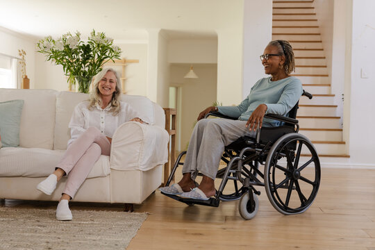 Senior friends having conversation at home, one on couch, one in wheelchair