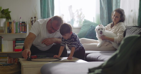 Family spending time together in cozy living room, grandfather playing with young boy, mother smiling with pet dog on couch, warm and homely atmosphere, bonding moment