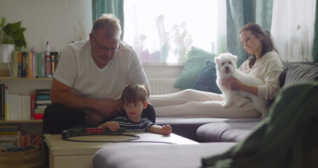 Fototapeta premium Family spending time together in cozy living room, grandfather playing with young boy, mother smiling with pet dog on couch, warm and homely atmosphere, bonding moment